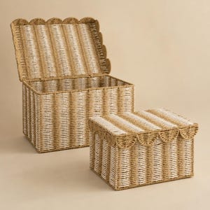 May include: Two rectangular storage baskets woven from natural tan and white fibers. The baskets feature vertical striped patterns and scalloped edges along the lids. One basket is shown with its lid open, while the other is closed.