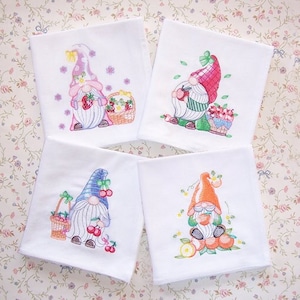 May include: Four white embroidered handkerchiefs featuring whimsical gnomes. Each gnome is depicted with a different hat and holding or surrounded by fruit, including strawberries, apples, and cherries. The embroidery is colorful and detailed.