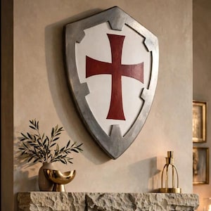 May include: A stone fireplace with a burning fire inside, featuring a large shield-shaped wall decoration above the mantel. The shield is silver with a white center and a red cross. The fireplace is constructed from rough-hewn, light-colored stone blocks.
