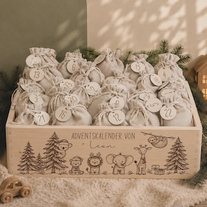 Peut inclure: Une boîte rectangulaire en bois contenant de nombreux petits sacs en tissu beige avec des cordons et des étiquettes en bois numérotées. La face avant présente des gravures d'arbres et d'animaux avec le texte "ADVENTSKALENDER VON Leon".