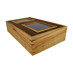 Könnte beinhalten: Eine Holzkiste mit zwei rechteckigen Glasfenstern auf der Oberseite. Die Kiste ist aus hellem und dunklem Holz mit einer natürlichen Holzoptik.