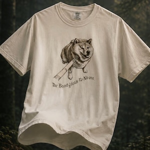 May include: A cream-colored short-sleeve t-shirt featuring a dark brown graphic of a dog holding a stick in its mouth. Below the dog, the text reads, "The Beast Yields To No one." The shirt has a crew neckline and a standard fit design.