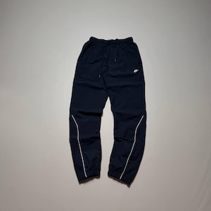 Può includere: Pantaloni sportivi blu navy scuro con vita elastica e coulisse, polsini alle caviglie e un piccolo logo Nike bianco sulla coscia sinistra. I pantaloni presentano sottili dettagli a contrasto bianchi che si curvano lungo la parte inferiore.