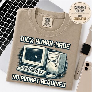 Könnte beinhalten: Ein sandsteinfarbenes T-Shirt mit einer Grafik eines Vintage-Computers, einer Tastatur und einer Maus. Der Text lautet 100% HUMAN-MADE und NO PROMPT REQUIRED in einer verpixelten Schriftart. Das T-Shirt hat ein Comfort Colors Markenetikett.