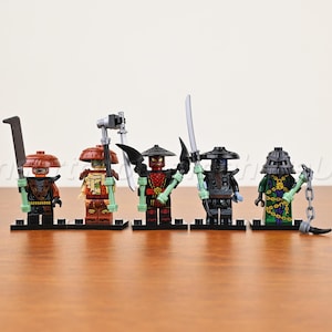 May include: Five plastic minifigures standing on black display bases. Each figure wears a wide-brimmed hat and carries a weapon, including swords, a scythe, and a chain. The characters feature detailed armor in red, black, and green color schemes.