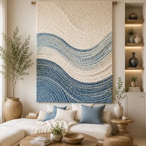 May include: A large rectangular wall hanging featuring a textured, tufted design with undulating wave patterns in shades of cream, light blue, and deep blue. The piece is suspended from a wooden rod and displays a dense, yarn-like surface texture.