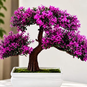 May include: An artificial bonsai tree with a textured brown trunk and vibrant magenta flowers. The tree is planted in a rectangular white ceramic pot with a green moss-like base, featuring a wide, spreading canopy of small, dense foliage.
