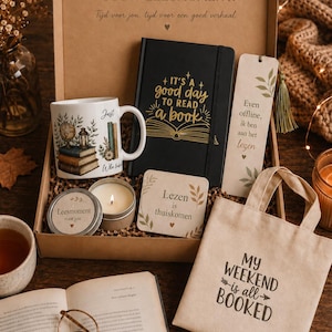 Op de afbeelding: Een geschenkdoos met een witte mok met boekenillustratie, een zwart notitieboek met de gouden tekst IT'S A GOOD DAY TO READ A BOOK, een boekenlegger, een kaars in een blikje, een vierkante onderzetter en een kleine beige tas met de tekst MY WEEKEND IS ALL BOOKED.