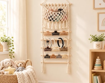 May include: A wall-mounted macrame organizer featuring a top woven pouch and five horizontal wooden dowels. The organizer holds various hair accessories, including plastic claw clips in neutral tones and several headbands arranged on the rods.