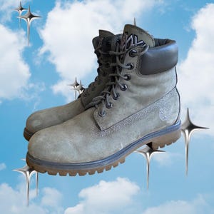 May include: A pair of olive green suede lace-up boots featuring a dark brown padded collar, dark metal eyelets, and a thick brown rubber lug sole. The side of the boot displays a debossed tree logo, and the tongue features a prominent black logo patch.