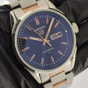 Peut inclure: Une montre automatique TAG Heuer Carrera avec un cadran bleu profond, des aiguilles et des index couleur or rose, et un guichet jour-date à trois heures. Le garde-temps est doté d'un bracelet à maillons bicolore en acier et or rose.