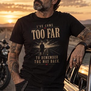 Puede incluir: Una camiseta negra de manga corta con el texto I'VE COME TOO FAR TO REMEMBER THE WAY BACK en letras color canela. El gráfico incluye la silueta de una persona con sombrero caminando por una carretera desértica bajo un cielo nublado al atardecer.