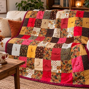 Peut inclure: Une courtepointe en patchwork composée d'une grille de carrés dans des tons de rouge, jaune, marron et crème, ornée de divers motifs floraux et géométriques. La courtepointe est finie avec une bordure rouge foncé et des nœuds en fil.