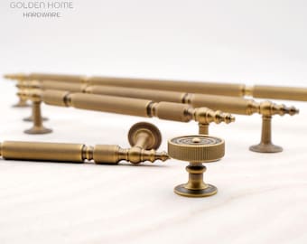 May include: A collection of antique brass cabinet hardware including long, cylindrical, textured bar pulls and a single round knob. The hardware features a knurled finish and tapered ends. The text GOLDEN HOME HARDWARE is visible at the top.