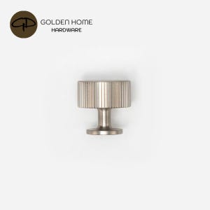 Op de afbeelding: Een kastknop van geborsteld nikkel met een cilindrische kop voorzien van verticale ribbeldetails en een gladde, smalle steel. Bovenaan de afbeelding staat het logo van GOLDEN HOME HARDWARE, inclusief een bruin rond icoon met de letters GH.