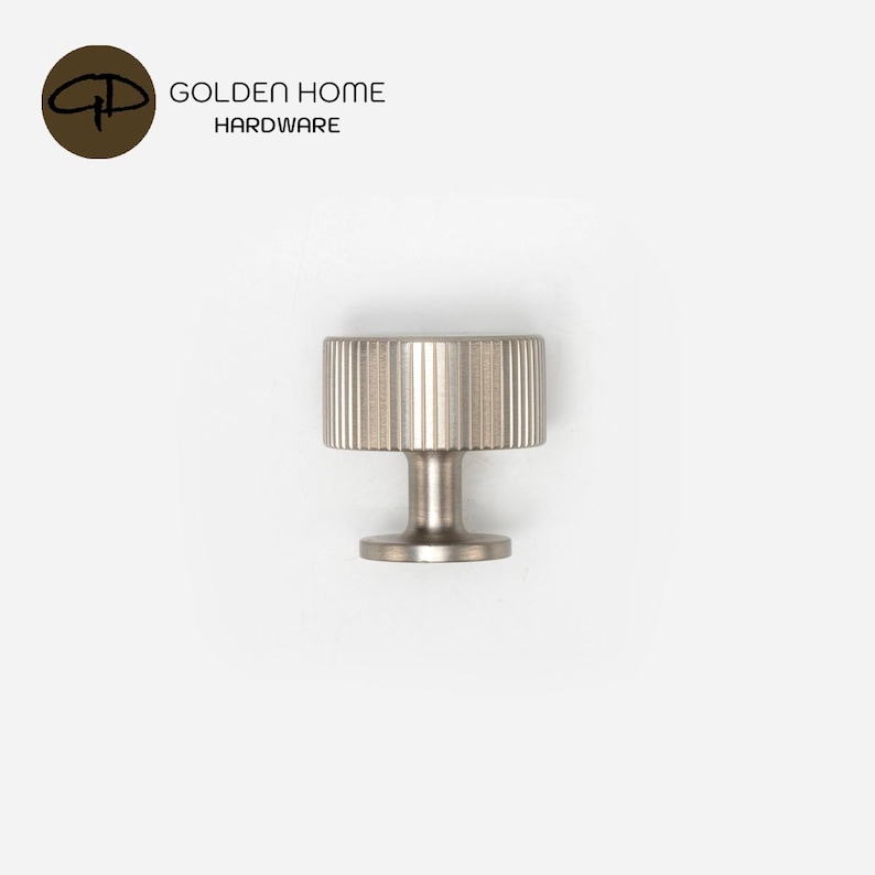 Op de afbeelding: Een kastknop van geborsteld nikkel met een cilindrische kop voorzien van verticale ribbeldetails en een gladde, smalle steel. Bovenaan de afbeelding staat het logo van GOLDEN HOME HARDWARE, inclusief een bruin rond icoon met de letters GH.
