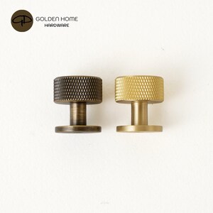 May include: Two cylindrical metal cabinet knobs with a textured diamond-patterned edge. One knob features a dark bronze finish, while the other has a bright brass finish. Both knobs include a central stem and a flat circular base for mounting.