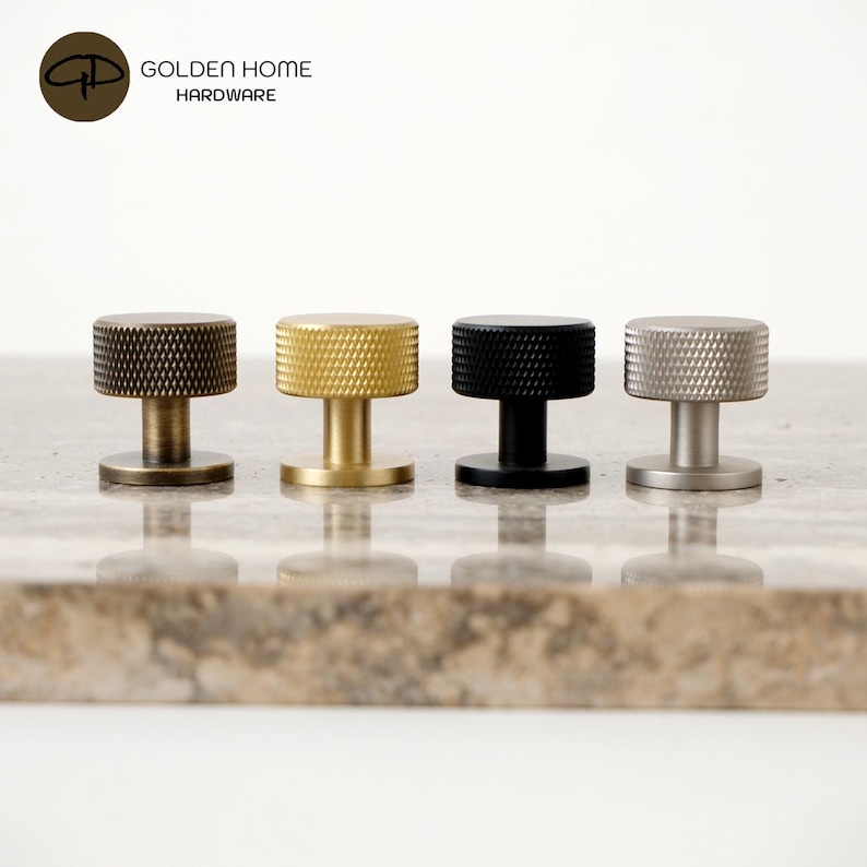 May include: Four cylindrical cabinet knobs with a textured, diamond-patterned knurled edge. The set includes one antique brass, one brushed gold, one matte black, and one brushed silver finish, each featuring a flat circular base and stem.