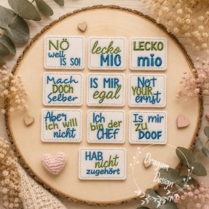 Könnte beinhalten: Zehn rechteckige, cremefarbene Stoffaufnäher mit abgerundeten Ecken, jeweils mit gesticktem deutschem Text in blauem und grünem Garn. Die Aufschriften lauten NÖ weil IS SO, lecko MIO, LECKO mio, Mach DOCH Selber, IS MIR egal, Not YOUR ernst, Aber ich will nicht, Ich bin der CHEF, Is mir ZU DOOF und HAB nicht zugehört.