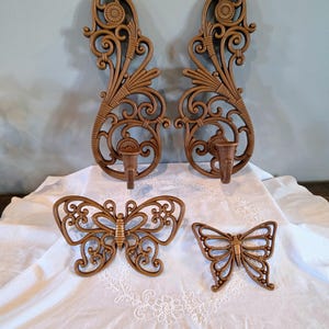 May include: A set of four brown wall-mounted items including two tall, vertical candle sconces with intricate scrollwork and floral motifs, and two butterfly-shaped wall plaques featuring openwork patterns and symmetrical wing designs.