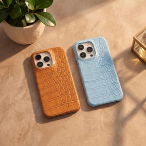 Peut inclure: Deux coques de smartphone avec un motif texturé en peau de crocodile. L'une est de couleur brun clair chaud et l'autre est bleu pastel clair. Les deux coques présentent une découpe pour un système de caméra à trois objectifs en haut à gauche.