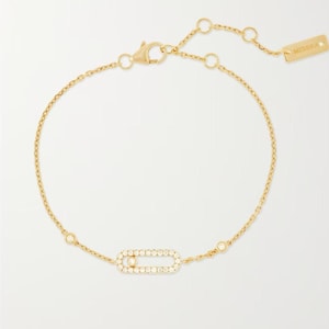 Könnte beinhalten: Ein goldenes Kettenarmband mit einem zentralen, ovalen Anhänger, der mit kleinen klaren Diamanten besetzt ist. Das Armband verfügt über einen Karabinerverschluss und ein kleines rechteckiges Schildchen mit der Gravur MESSIKA am Kettenende.