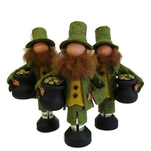 May include: Three felt leprechaun figures, each with a green top hat, green coat, and a long red beard. They hold a black pot filled with gold coins. The figures stand on black bases and have a yellow vest.