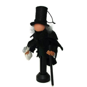 May include: A black felt doll wearing a black top hat, a black coat, and holding a walking stick. The doll has a white beard and a white bag in its hand.