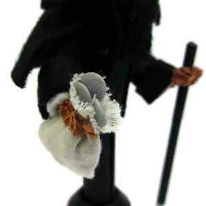 May include: A small, black-clothed figure with a white bag and a stick. The figure is wearing a white collar and has a brown fur trim around the bag.