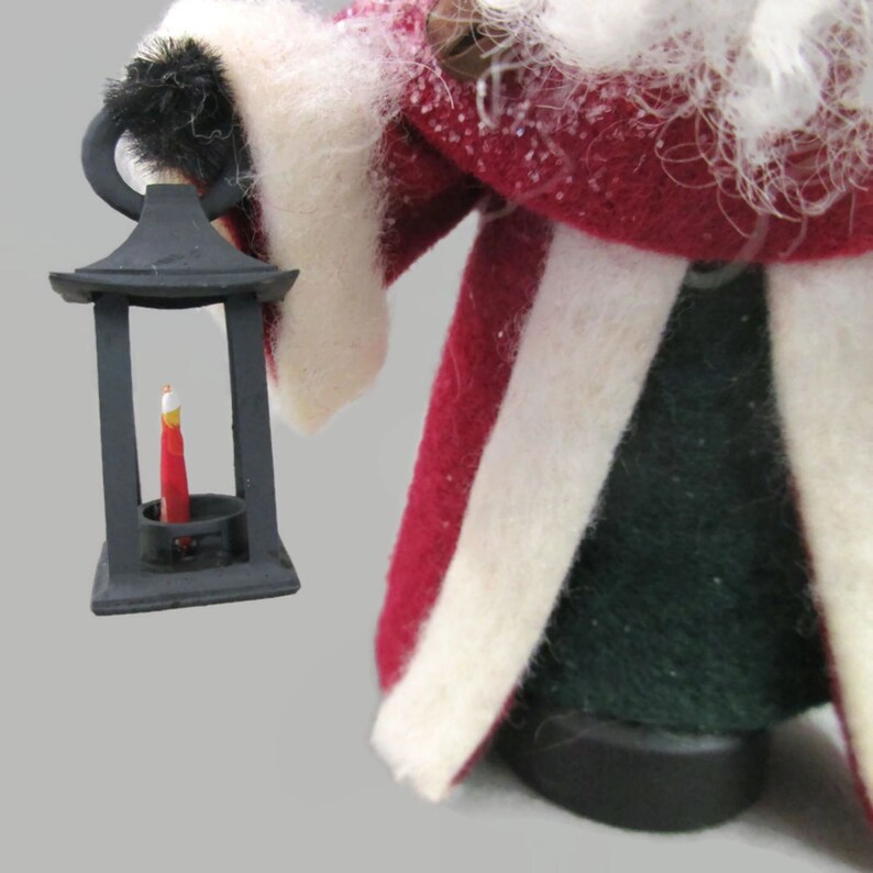 May include: A Santa Claus figurine holding a black lantern with a red candle inside. The figurine is wearing a red and white suit with a white fur trim.