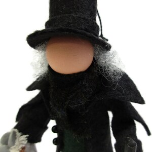 May include: A felt doll wearing a black top hat, black coat, and a white beard. The doll has a round, light brown face.