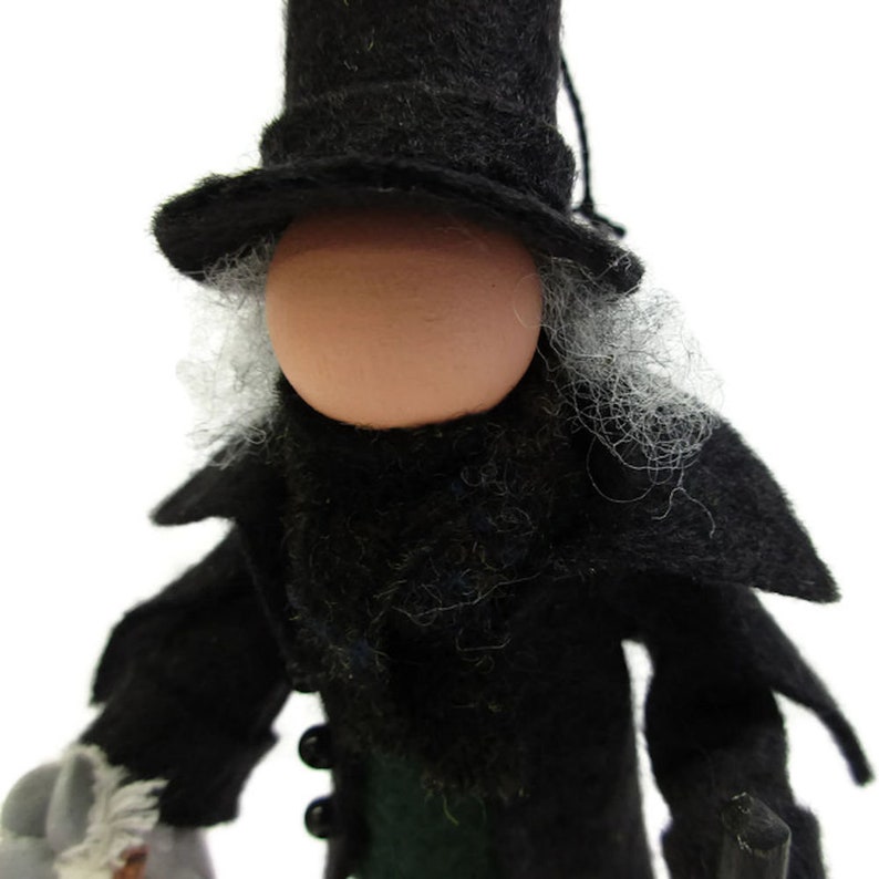 May include: A felt doll wearing a black top hat, black coat, and a white beard. The doll has a round, light brown face.