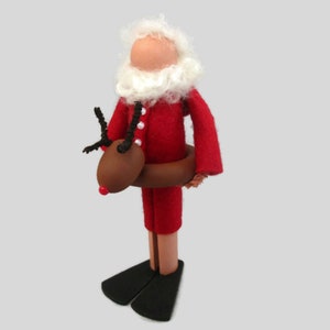 May include: A handmade felt Christmas ornament depicting Santa Claus wearing a red suit and a white beard, riding a brown reindeer with black antlers. Santa is wearing a brown inflatable ring around his waist.