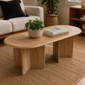 May include: An oval coffee table made of light-toned wood with a smooth surface and a sturdy base featuring intersecting panels. The table is positioned centrally, providing a flat surface for items like a potted green plant and stacked books.