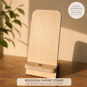 Op de afbeelding: Een lichtgekleurde houten telefoonstandaard met een glad, verticaal achterpaneel en een horizontale basisrand met een kleine ronde uitsparing. De afbeelding bevat de tekst DIGITAL DOWNLOAD CNC FILES DXF SVG PDF en WOODEN PHONE STAND.