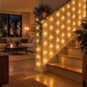 Puede incluir: Una cadena de luces LED en forma de estrella de color blanco cálido que cuelga verticalmente a lo largo de una barandilla de escalera de madera. Las luces están dispuestas en varios hilos paralelos, creando un efecto de cortina brillante.