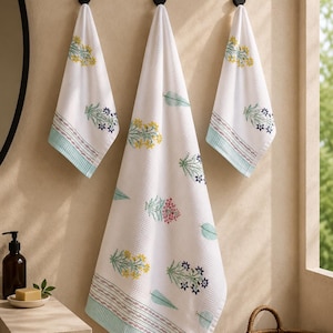 May include: Three white waffle-weave towels featuring a repeating botanical print of yellow, blue, and pink flowers with green leaves. Each towel has a decorative border with thin horizontal lines and a light teal band at the bottom edge.