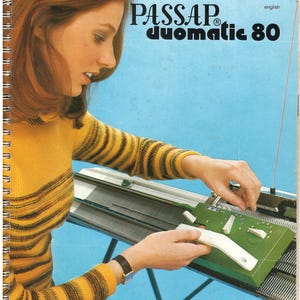 May include: A Passap Duomatic 80 knitting machine manual cover featuring the text Passap Duomatic 80 in black lettering. The cover displays a person wearing a yellow and brown striped long-sleeve sweater while operating the green machine.