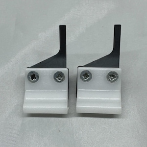 May include: Two white plastic and metal components with black blades and silver screws. The components are positioned side by side against a white background. The blades are angled and extend upwards.