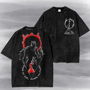 May include: A black acid-wash t-shirt featuring a graphic on the back of a knight figure surrounded by a red flaming circle and the text "BORN OF ASH, BOUND TO FLAME." The front chest area displays a smaller white graphic of a sword in a fire.