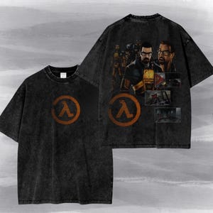 May include: A black acid-wash t-shirt featuring a circular orange Lambda logo on the front. The back displays a large graphic of a character with glasses, a yellow and black suit, and smaller rectangular scenes from a video game environment.