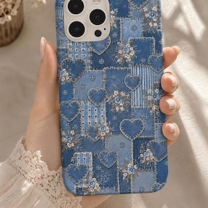 May include: A blue smartphone case featuring a patchwork design of denim-textured squares and hearts. The pattern includes various shades of blue, white stripes, and small floral accents scattered across the surface, with a camera cutout.