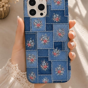 May include: A rectangular smartphone case featuring a blue denim patchwork design with visible white stitching. Each denim square is decorated with a small floral print consisting of tiny pink and light blue flowers with green leaves.