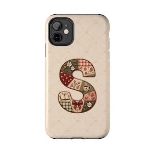 May include: A smartphone case with a cream-colored quilted background featuring a large letter S. The letter is composed of various patchwork-style fabric patterns including floral prints, red hearts, a coffee cup, an open book, and a red bow.