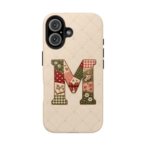 May include: A cream-colored phone case with a quilted diamond pattern featuring a large letter M in the center. The letter is decorated with a patchwork design of red hearts, green gingham, white daisies, a small red bow, a book, and a coffee cup.