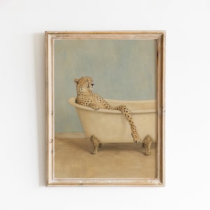 May include: A framed wall art print featuring a cheetah with its eyes closed, resting inside a cream-colored clawfoot bathtub. The cheetah is positioned with one leg extended over the edge of the tub. The background is a solid light blue color.
