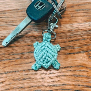 May include: A teal crocheted turtle keychain attached to a silver key ring and a car key with a Honda logo.