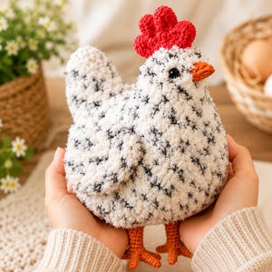 Può includere: Un giocattolo a forma di gallina realizzato all'uncinetto con un corpo bianco a macchie nere, una cresta rossa brillante e testurizzata e un becco arancione. La figura presenta due zampe e piedi arancioni, con una consistenza morbida.