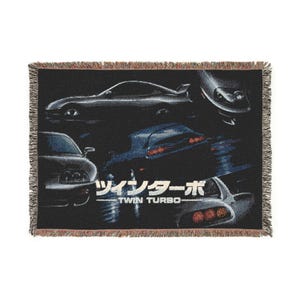May include: A rectangular woven throw blanket with a black background featuring multiple views of a sports car. The design includes the Japanese text "ツインターボ" and the English text "TWIN TURBO" in white. The blanket has a fringed edge.
