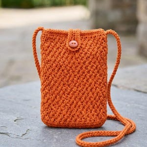 Könnte beinhalten: Eine leuchtend orangefarbene Häkel-Umhängetasche mit einem strukturierten, diagonalen Stichmuster. Die rechteckige Tasche verfügt über einen einzelnen, passenden orangefarbenen Knopfverschluss oben in der Mitte und einen langen, dünnen Häkelriemen.